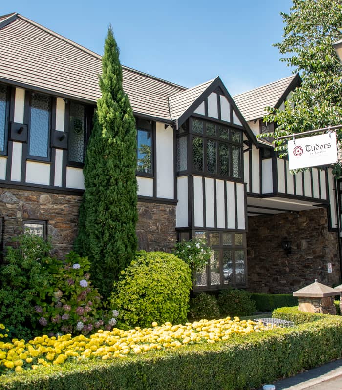 Hotel king bedroom with white bedding, decorative pillows, two nightstands, lamps, wall art, and a round mirror.