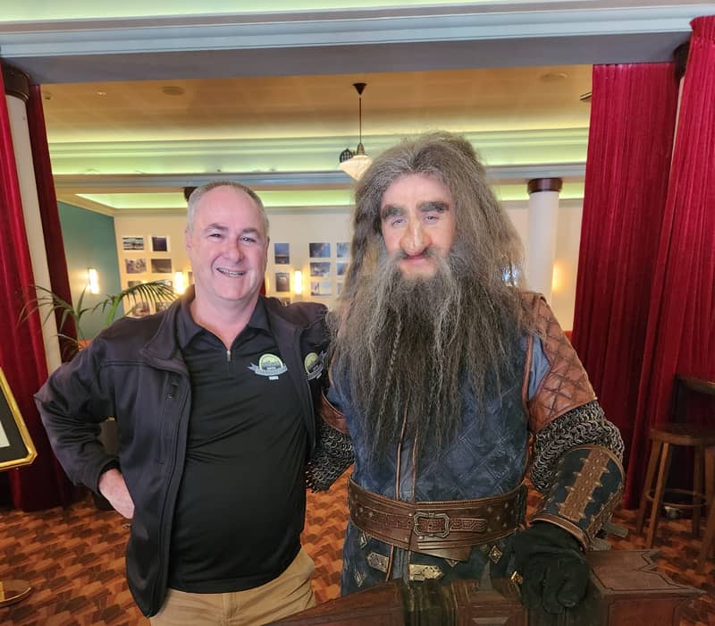 A tour guide standing next to a person in a detailed dwarf movie costume.