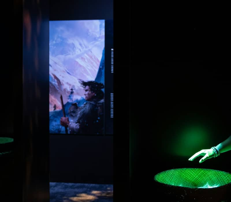Two women interacting with illuminated cultural exhibits in a dark museum room.