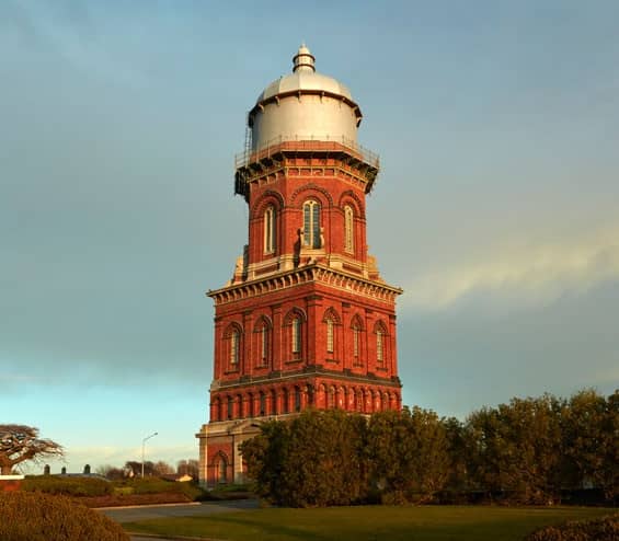 Historic red brick water tower at sunset surrounded by greenery in Invercargill. Credit: Fine Tours Group