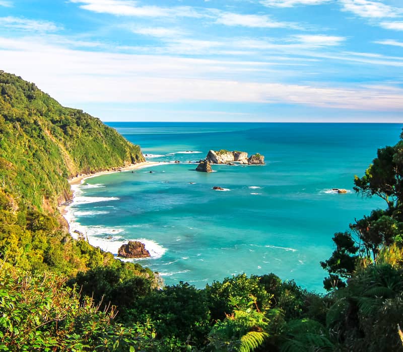Blue sky background with a Rainforest mountain in the foreground that meets the turquoise blue sea. 