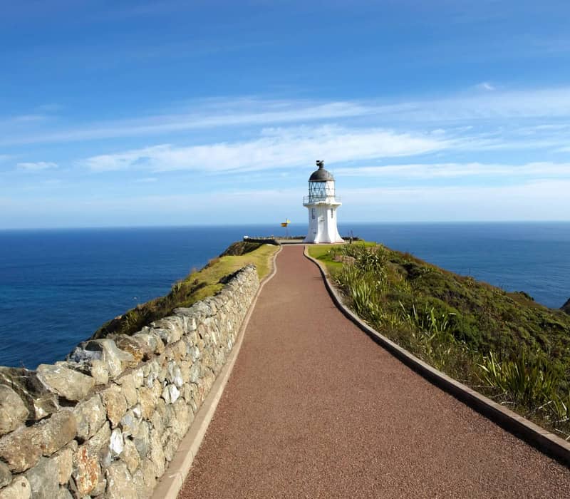 Path leading to Cape Reinga Lighthouse on a cliff overlooking ocean under blue sky