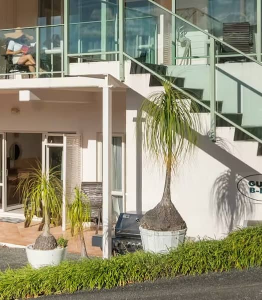 Outdoor area of Admirals View Lodge with balcony seating, patio chairs, potted plants, stairs, and barbecue facilities.