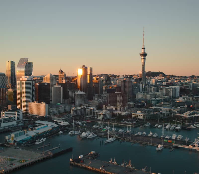 Sunset over Auckland city skyline with waterfront and boats in the harbor.