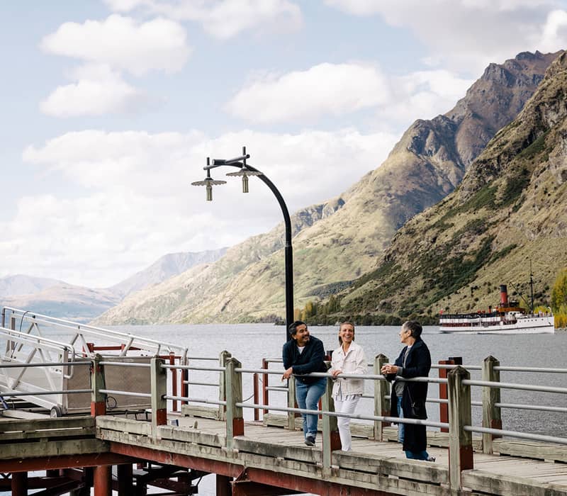 Visitors on a pier overlooking a lake with a steamship at Walter Peak High Country, Queenstown.