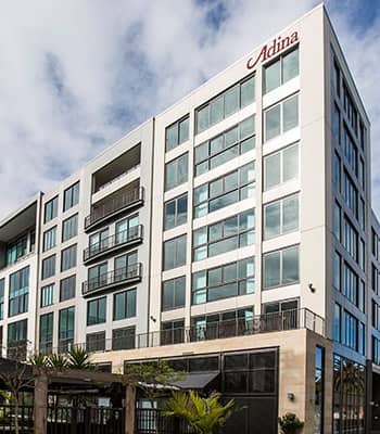 Modern multi-story hotel building with glass windows and balconies under a partly cloudy sky.