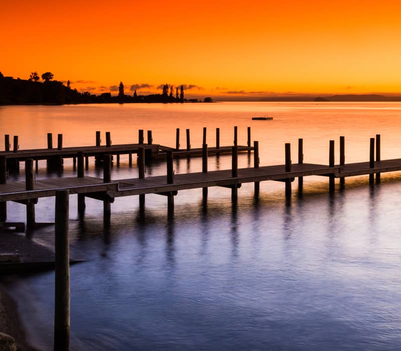 Wooden jetties on Lake Taupo at sunset with orange sky reflecting on calm water.