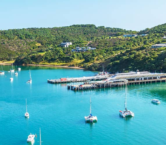 Waiheke Island's turquoise bay with sailboats and green hills.