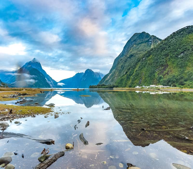 Milford Sound fjord with mountains reflected in calm water under a cloudy sky.