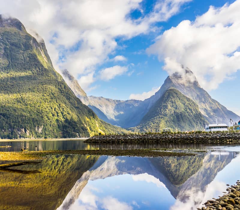 Mountains and clouds reflecting clearly in calm water at Milford Sound, New Zealand.