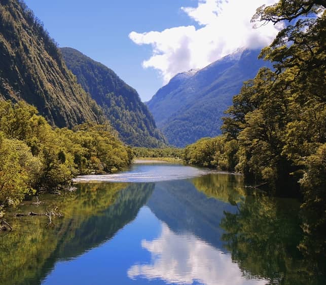 Calm river reflecting mountains and trees in Arthur Valley on the Milford Track, Fiordland.