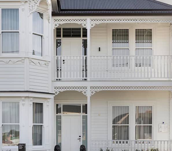 The exterior of a grand two-story white heritage villa with ornate woodwork and verandas.