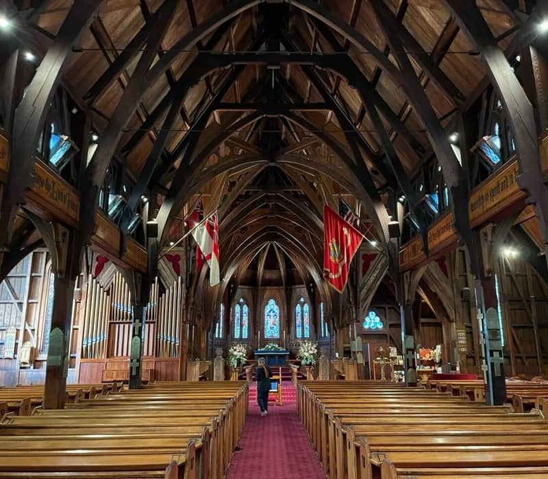 Interior of St Paul's Cathedral with wooden ceiling, pews, stained glass, and flags.