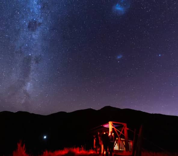 Group of people under starry night sky with Milky Way near a zipline platform lit by red light