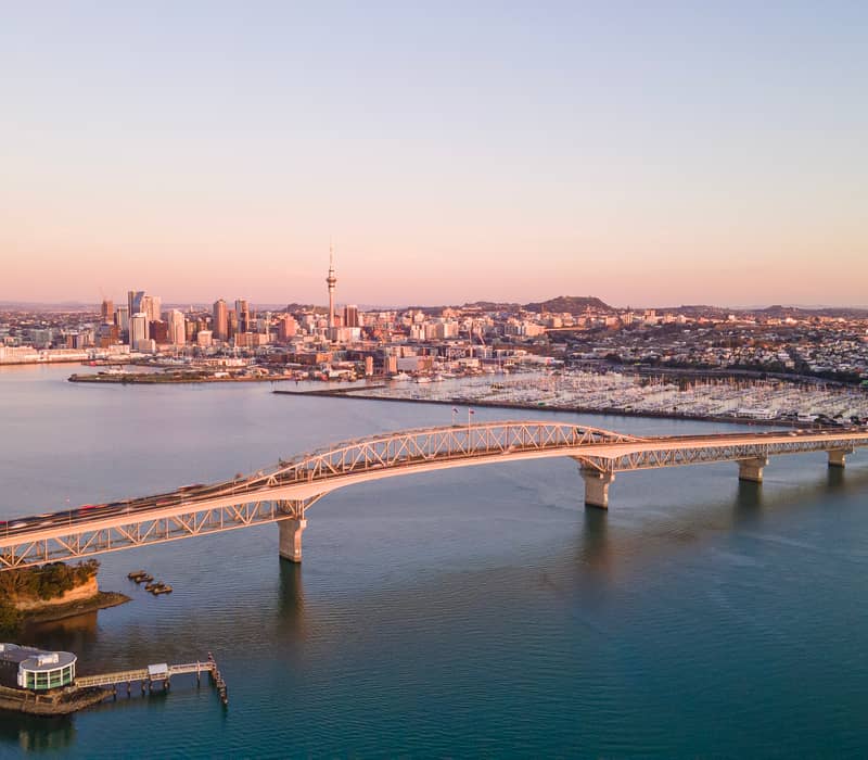 Aerial view of Auckland city skyline with bridge and harbor at sunset.