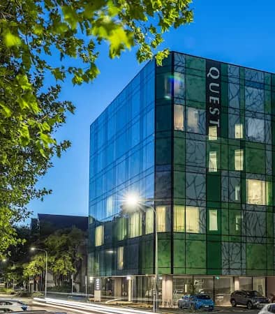 Modern glass facade hotel building illuminated at night with trees and parked cars nearby.