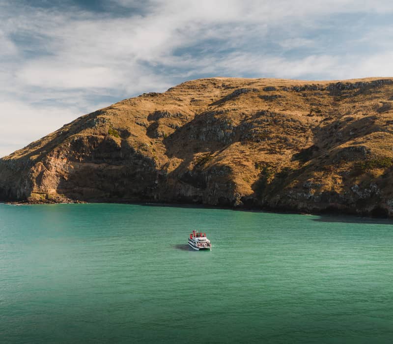 Boat on green water near rocky cliffs under blue sky with clouds.