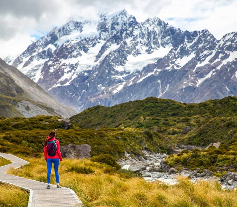 A person in bright colourful clothing standing on the walkway with Mt Cook in the background 