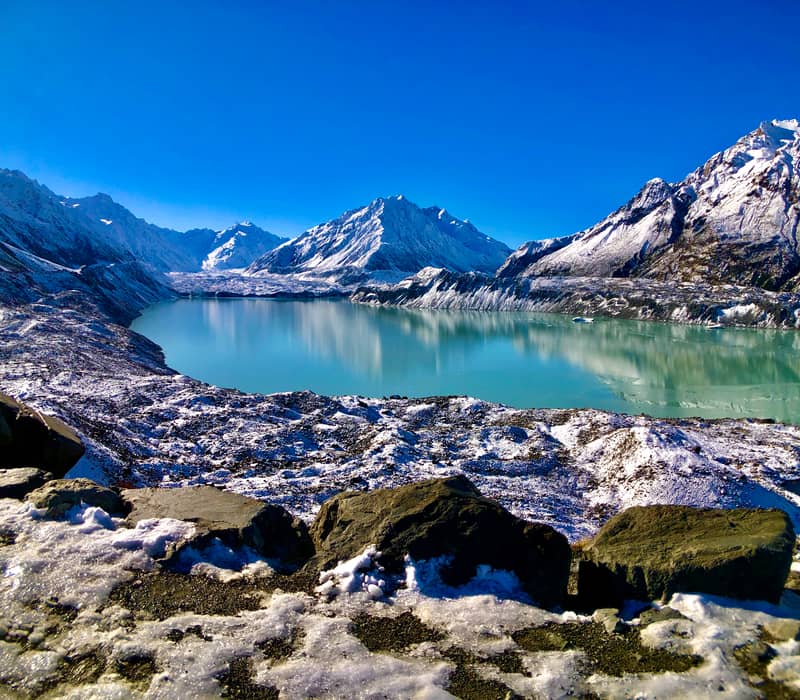 Glacial lake with snowy mountains and rocks under clear blue sky