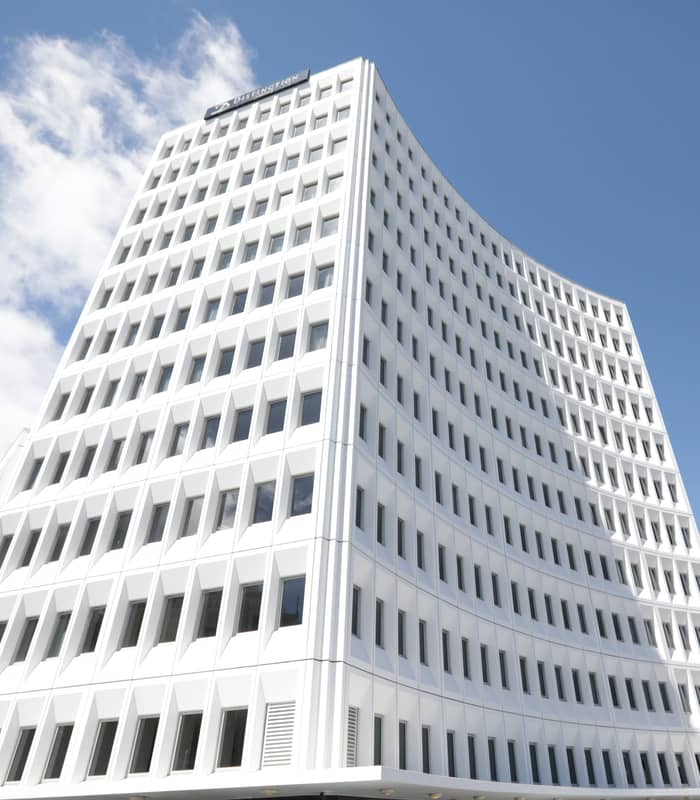 White modern hotel building with rows of windows against blue sky and clouds.