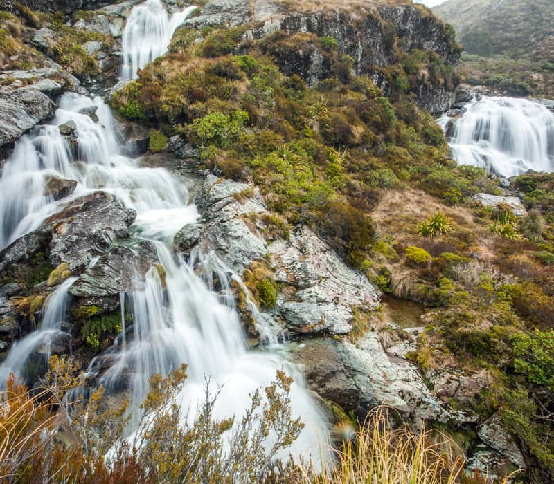 Waterfalls flowing over rocks with green shrubs and moss on a mountain landscape