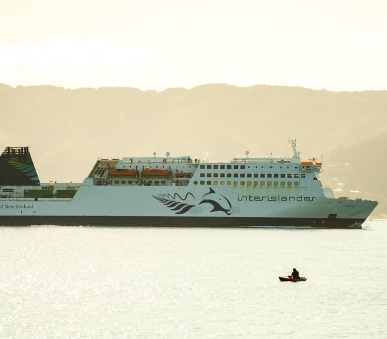 Interislander ferry Kaitaki with a kayaker on the water in front of mountain landscape