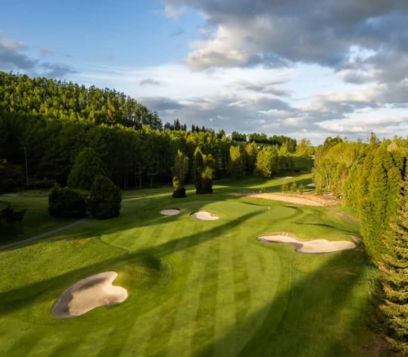 An aerial view of the lush green fairway and sand bunkers of Wairakei Golf + Sanctuary under a partly cloudy sky at sunset. Credit: Wairakei Golf Club