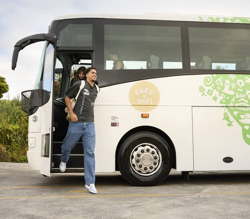 Young man stepping off an intercity bus with a free WiFi sign and green designs on its side during the day.