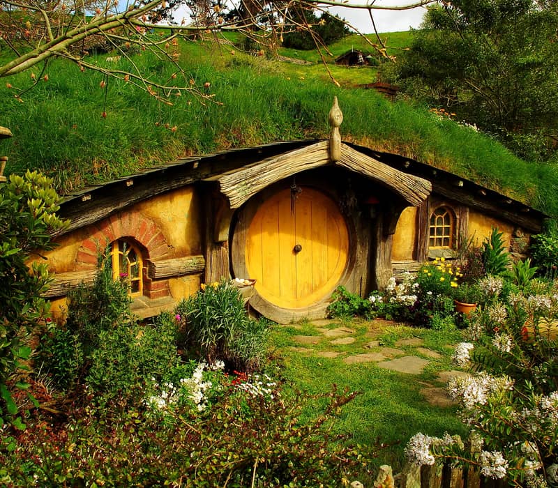 Hobbit house with round red door surrounded by flowers and greenery in Hobbiton