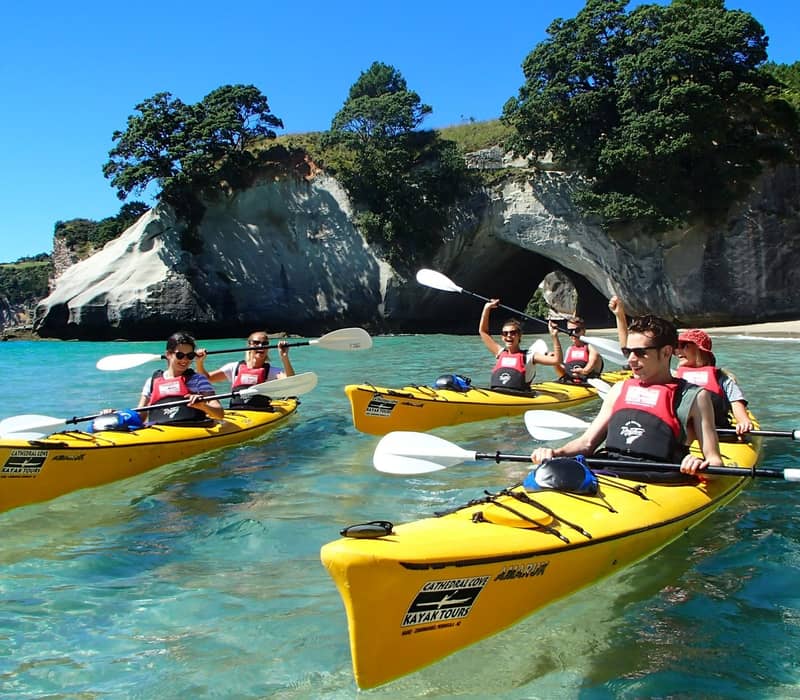 Group kayaking in yellow kayaks near rock formations and clear water on a sunny day.