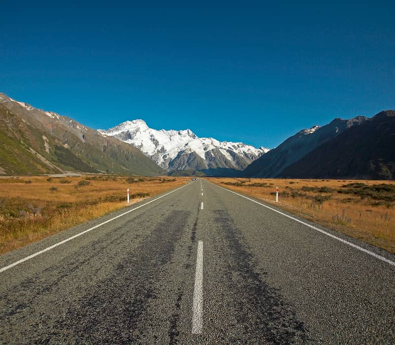 Road stretching towards snow-capped Aoraki Mount Cook with mountains and clear blue sky