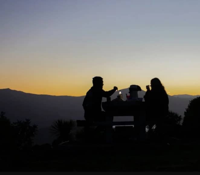 Silhouettes of two people having a picnic at sunset with mountains in the background. Credit: Akaroa Stargazing