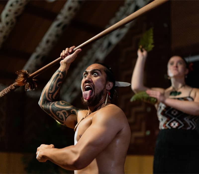 Maori warrior performing a traditional haka with spear and fierce expression. Credit: Te Puia