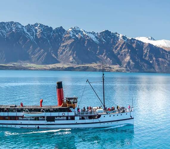 Steamship on lake with snow-capped mountains in New Zealand.