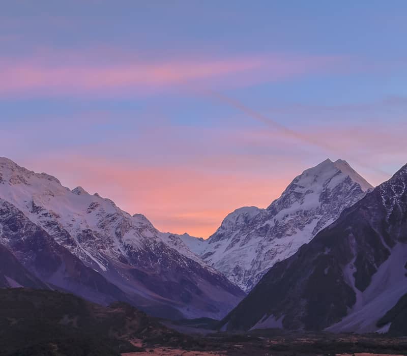 Snow-covered mountain peaks of Aoraki Mount Cook at sunset with a colorful sky.