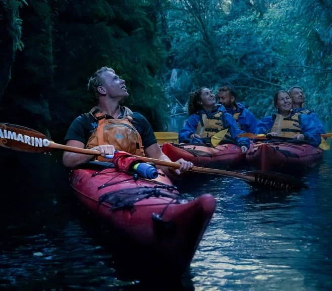Group kayaking inside a dark cave with life jackets and paddles on calm water