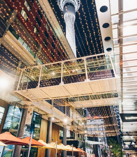 Hotel suite with king bed, red armchairs, flat-screen TV, and city view at sunset.