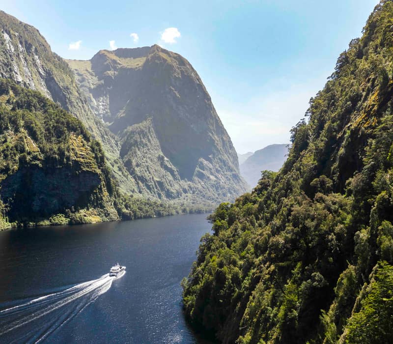 Boat traveling through a fjord with green mountains and clear blue sky