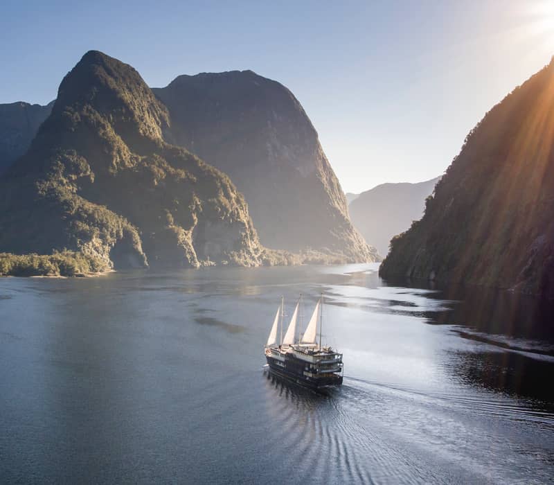 Boat traveling through a fjord with green mountains and clear blue sky