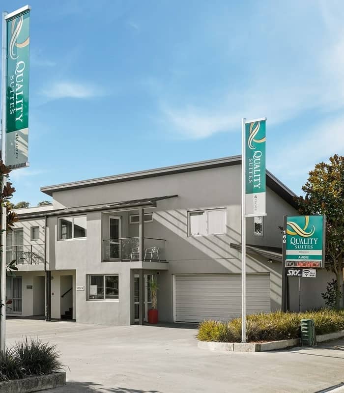 Modern hotel building with signage and parking lot under clear blue sky.
