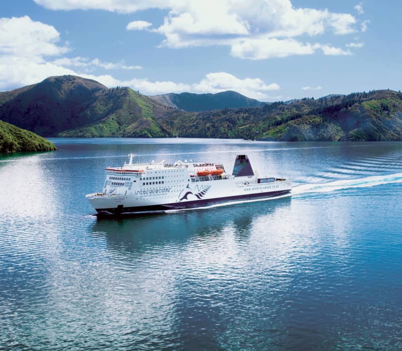 Ferry sailing on calm water with mountains and blue sky in the background. Credit: Interislander