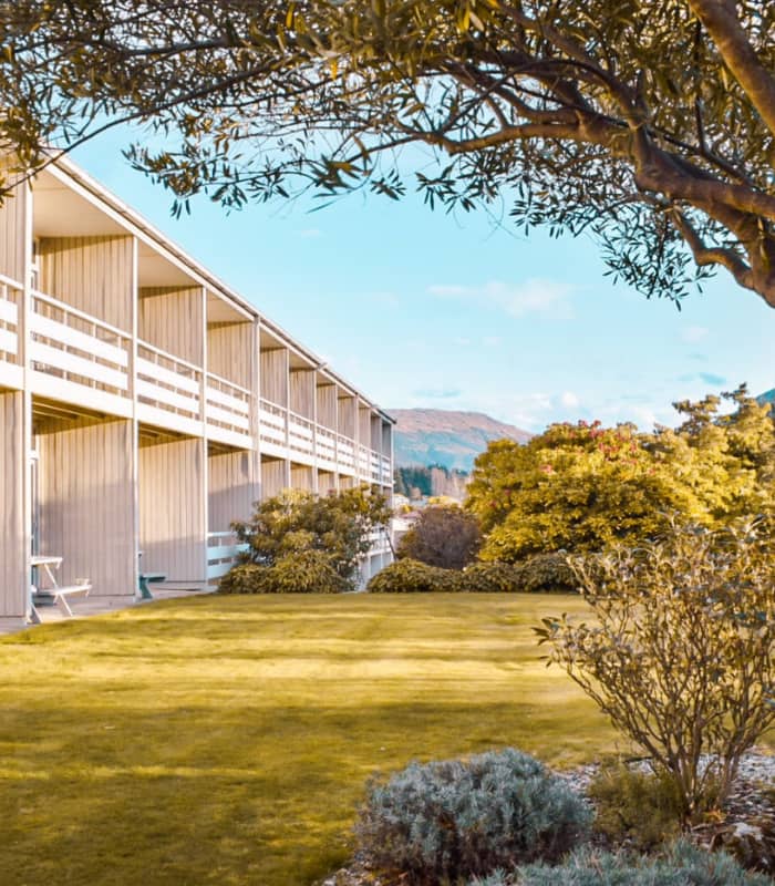 Outdoor garden and lawn area with trees and hotel balconies under a blue sky.