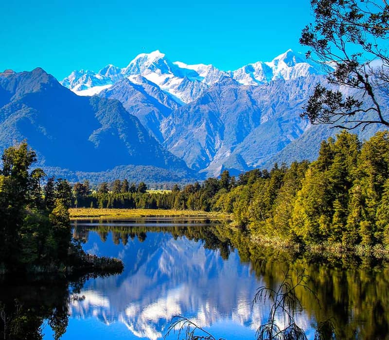 Snow-capped mountains and forest reflected in a clear lake, South Island, New Zealand.