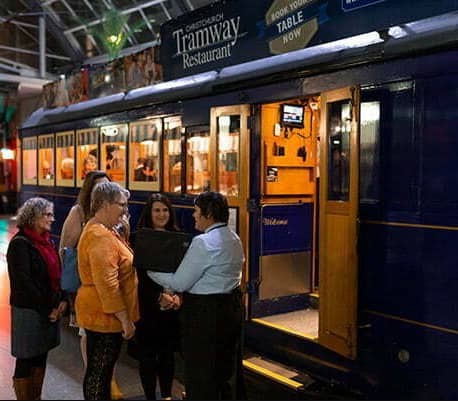 People standing at the entrance of the Christchurch Tramway Restaurant tram at night.