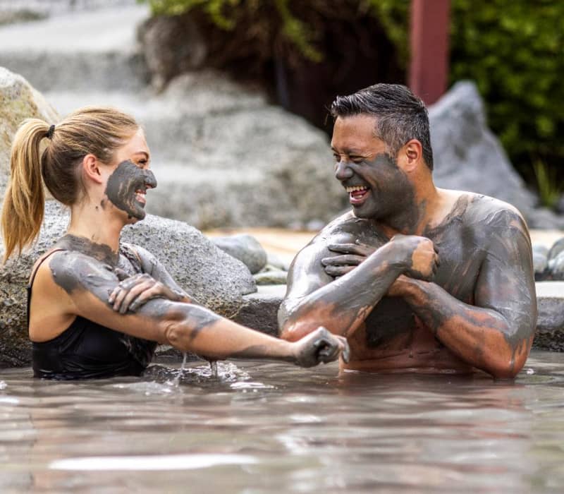 Happy couple covered in mud enjoying a mud bath outdoors, smiling and having fun.