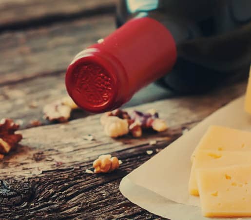 Wine bottle, sliced cheese, and walnuts on a rustic wooden table.