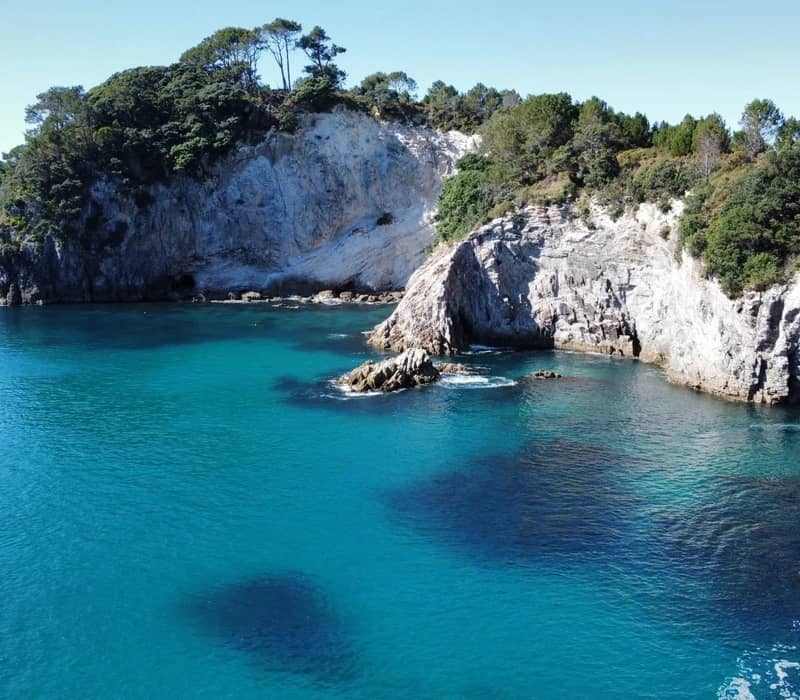 Boat near rocky cliffs and clear turquoise water at Cathedral Cove on a sunny day.