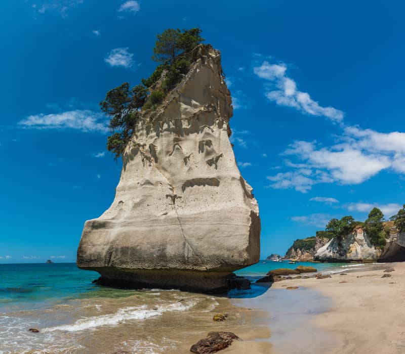 Tall rock formation on sandy beach with blue ocean and sky at Cathedral Cove, Coromandel