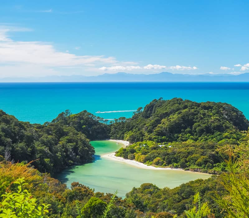 Lush green headlands surrounding a bright turquoise lagoon and white sand beach in New Zealand.