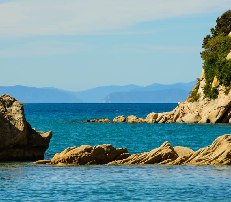 Large granite boulders and rock formations on the edge of a clear blue ocean.